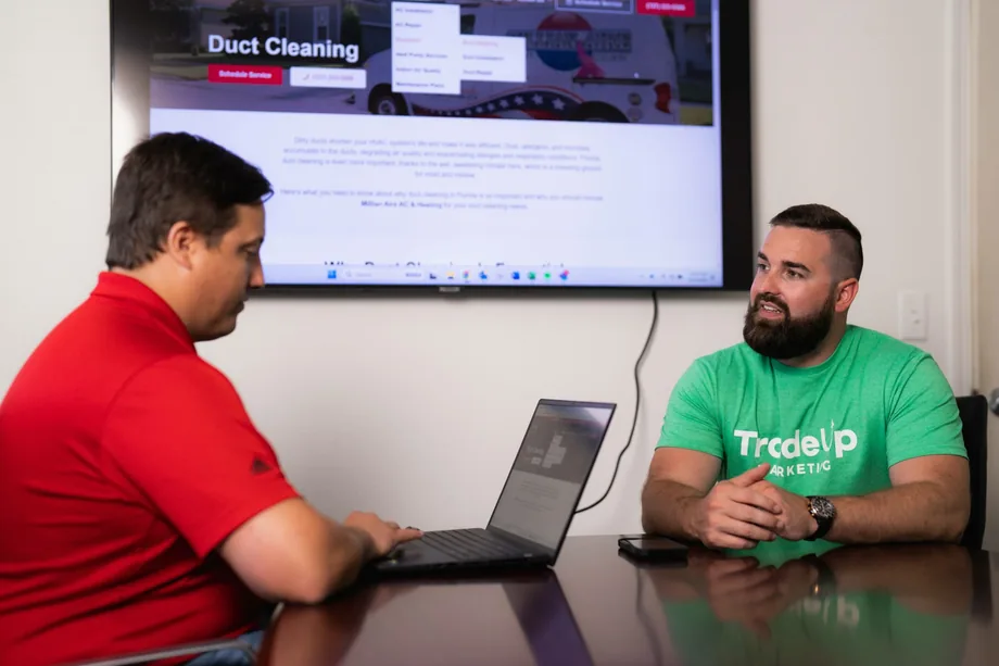 TradeUp Marketing strategist reviewing a duct cleaning website with a client on a wall screen