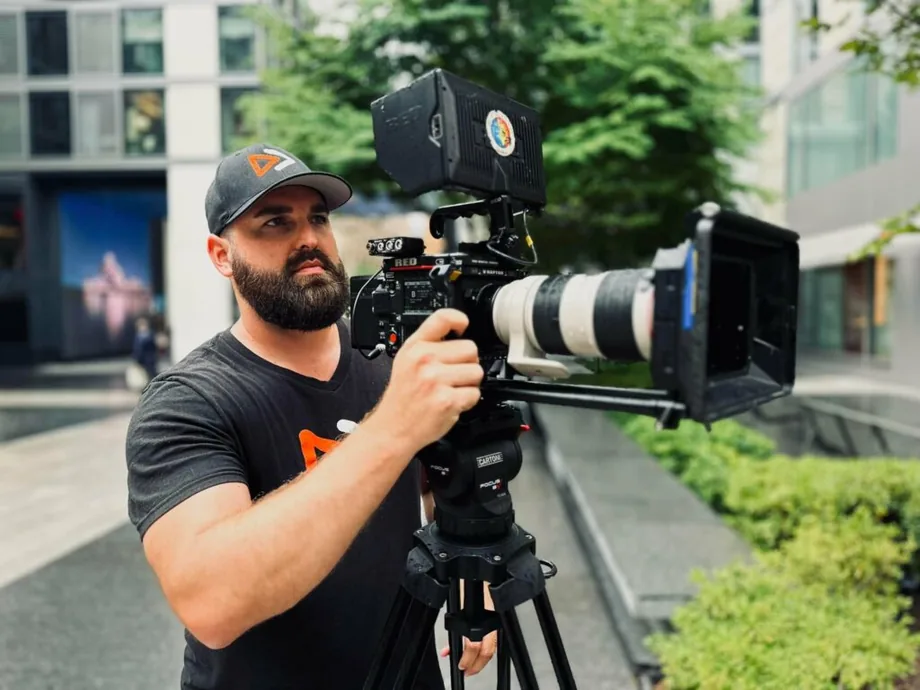 Jordan Lung operating a cinema camera with a telephoto lens on location