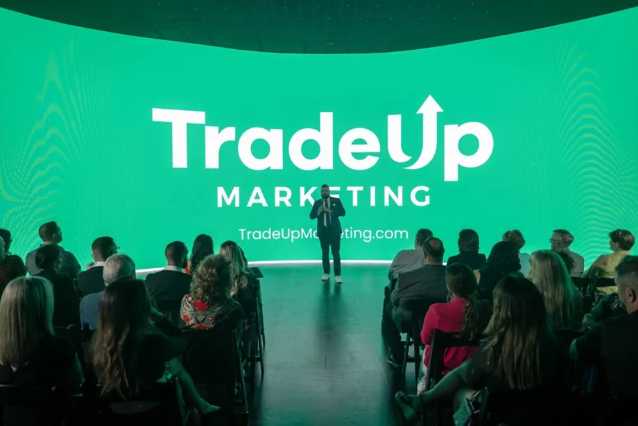Jordan Lung on stage in front of a TradeUp Marketing screen with a seated audience