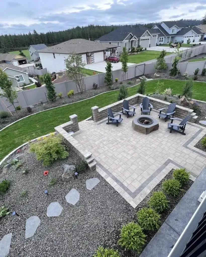 Greenscape project photo — a raised paver patio with a stone fire pit and Adirondack chairs, edged by a gravel bed with stepping stones