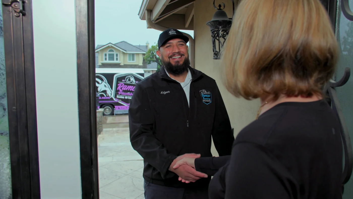 Ramco project photo — a Ramco technician in a branded jacket and cap shaking a customer’s hand at her front door, the wrapped van on the drive behind him