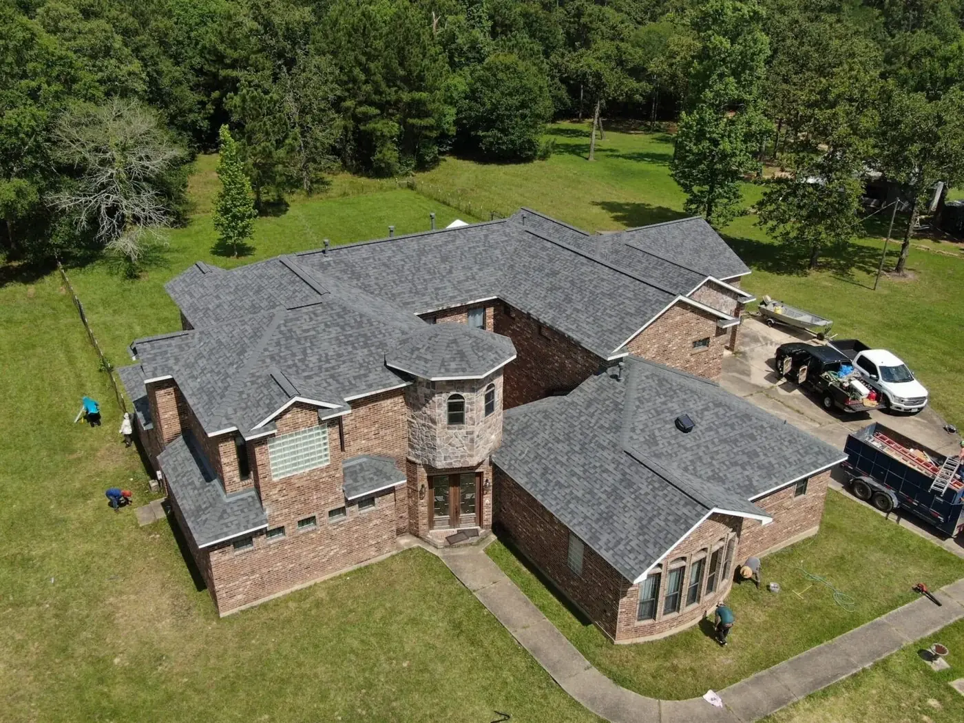Roof Ryders project photo — a drone view of a large brick home in Lufkin, Texas with a new grey shingle roof, the crew and trailer still on site