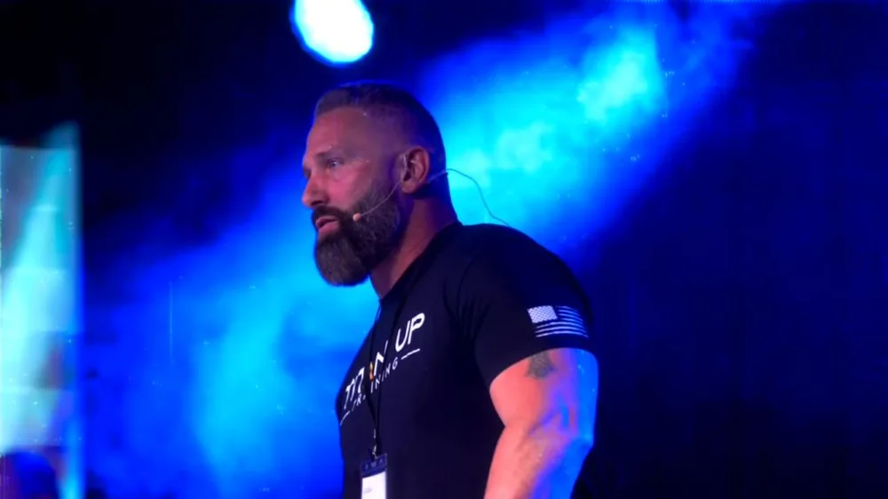 Regan Weiss speaking on stage under blue lighting with a headset microphone